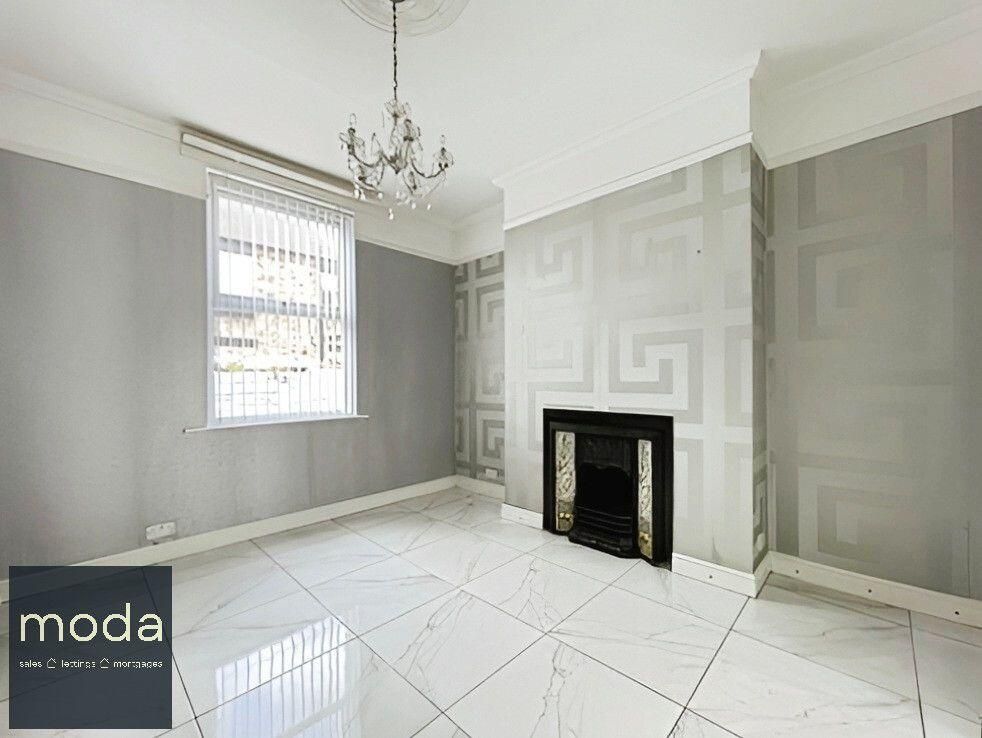 Empty living room with silver patterned wallpaper, fireplace, chandelier, and white tile floors.