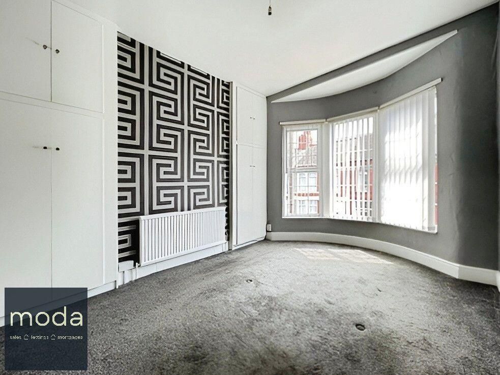 Empty bedroom with patterned accent wall and bay window, gray carpet, and white built-in cabinets.