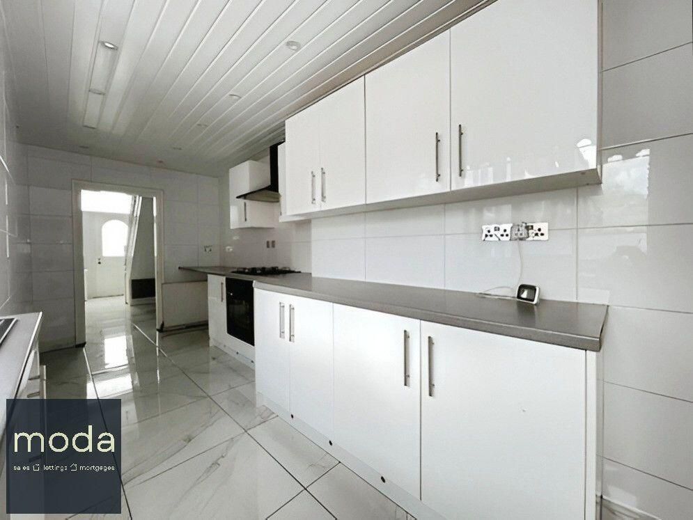 Modern white kitchen with stainless steel countertops and glossy cabinets.
