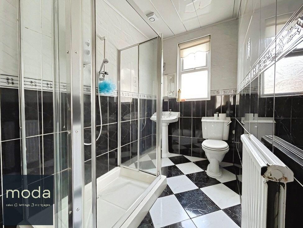 Bathroom with black and white checkered floor, shower, toilet, sink, and window.