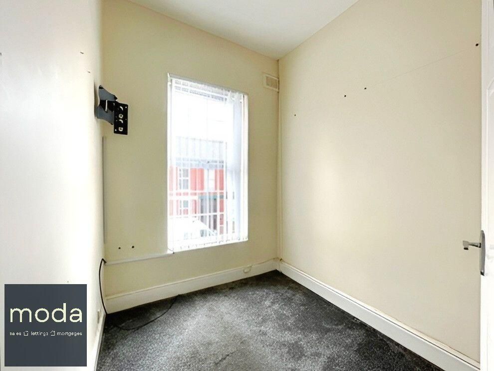 Empty room with window.  Beige walls, dark carpet. A mounted TV bracket.
