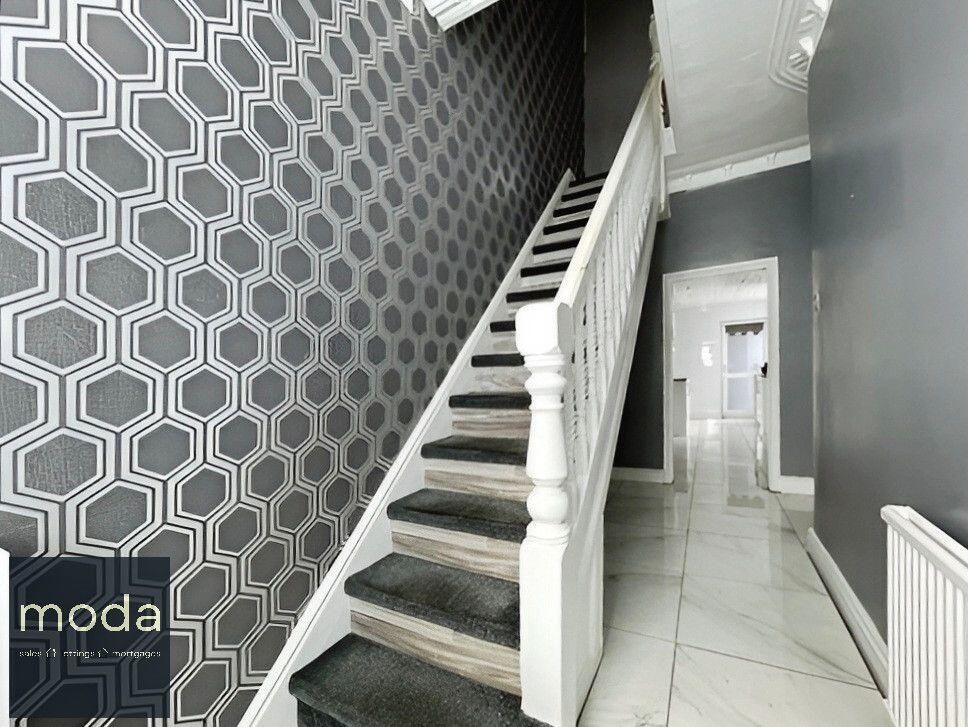 A staircase with gray carpet and white railing, gray hexagonal wallpaper on the left wall, and a hallway on the right.