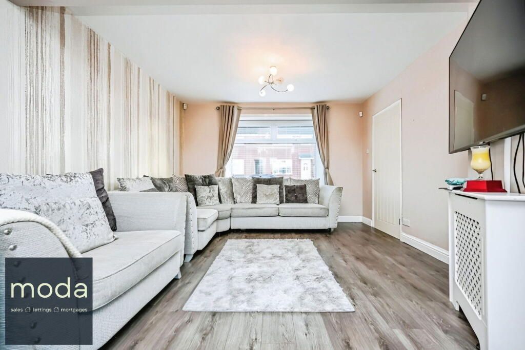 Cozy living room with gray sectional sofa, floral rug, and wood-look flooring; window with curtains.