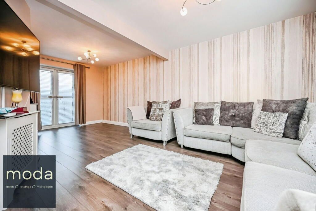 A living room with light-colored sectional sofa, area rug, striped wallpaper, and balcony doors.