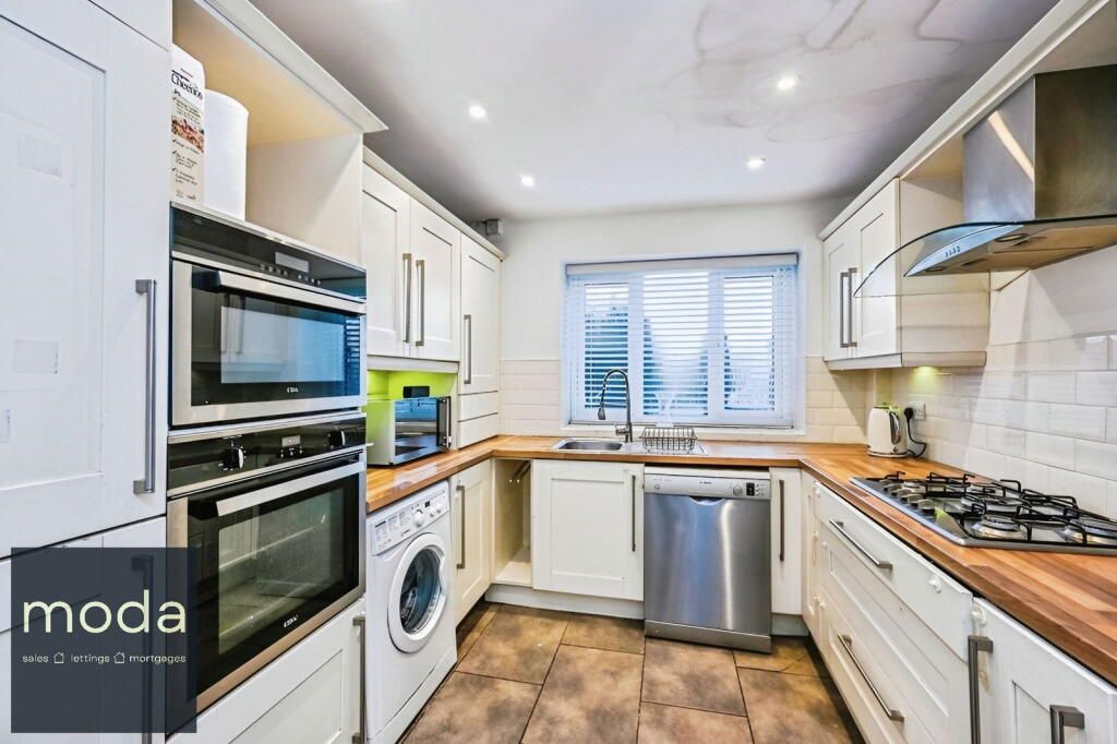 Small, white kitchen with wood countertops, stainless steel appliances, and a window.