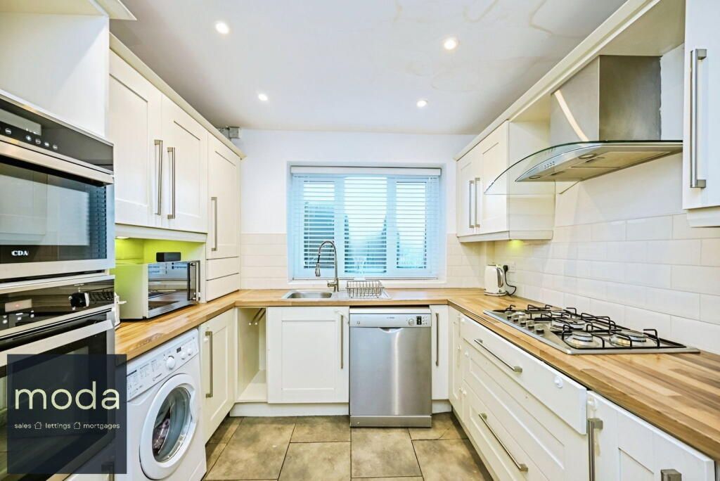 U-shaped kitchen with white cabinets, wooden countertops, stainless steel appliances, and a window with shutters.