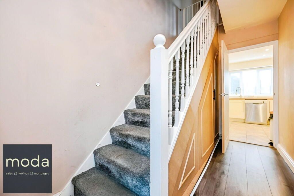 Staircase with carpeted steps, white banister, and hallway leading to a kitchen.