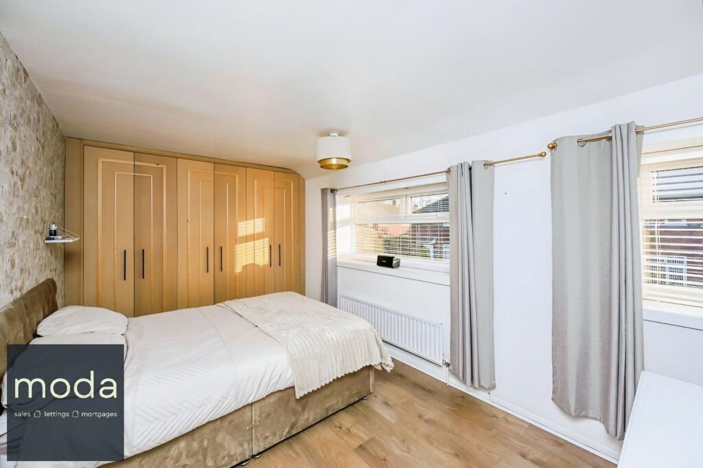 Bedroom with wooden floor, large wardrobe, bed, windows with curtains, and a light fixture.