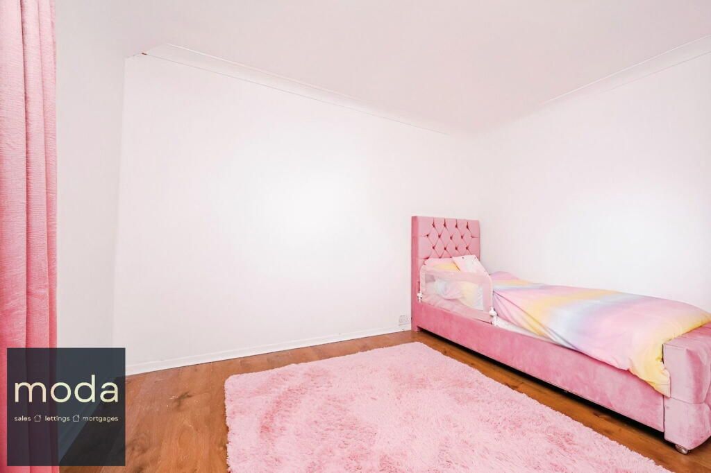 Pink bedroom with bed, rug, curtains, and hardwood floor.