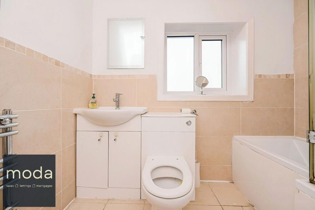 Bathroom with toilet, sink, and tub. Beige tiles and white fixtures, window with small mirror.
