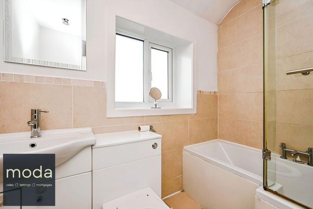 Bathroom with beige tile, white fixtures, window, sink, toilet, and bathtub.