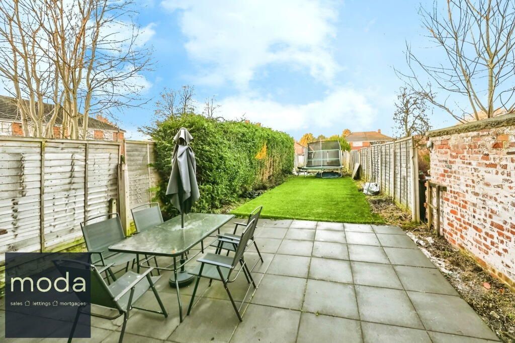 Backyard patio with table and chairs, lawn, hedges, and brick wall.