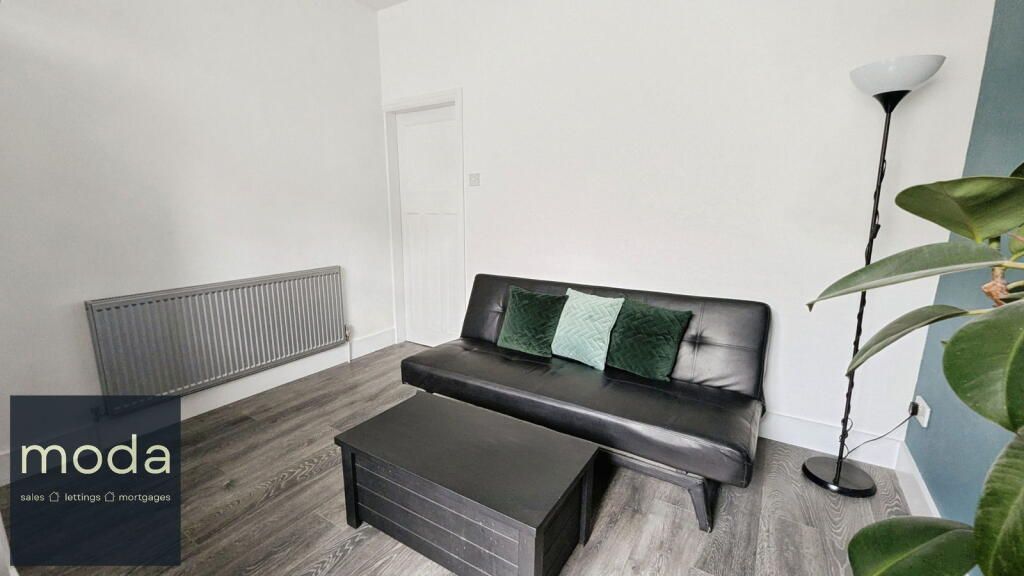 Living room with black couch, coffee table, floor lamp, and plant. Gray wood-look floor and white walls.