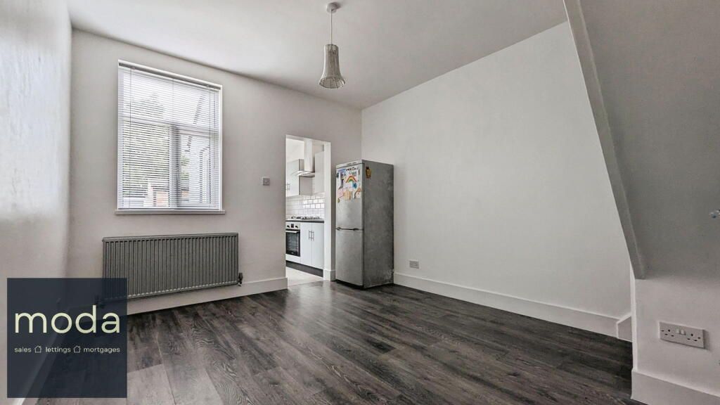 Empty studio apartment with dark wood floors, white walls, and a stainless steel fridge.