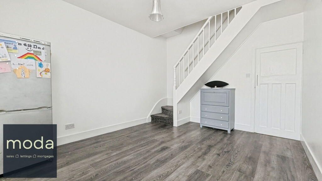 Empty room with stairs, light gray chest, refrigerator, and white walls/trim, dark floor.