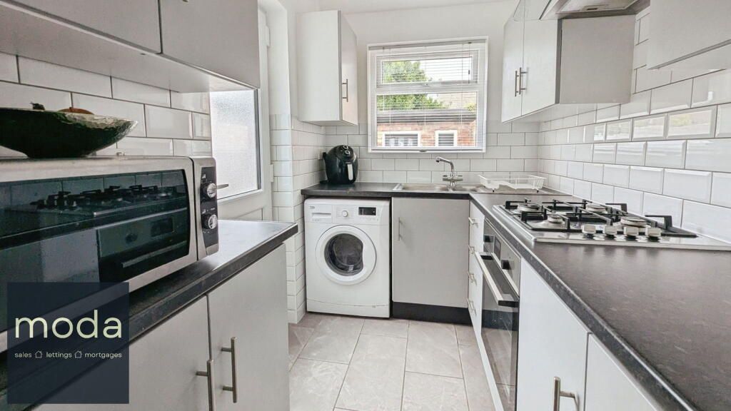 Small kitchen with white cabinets, subway tile, and dark countertops, with a washing machine and oven.