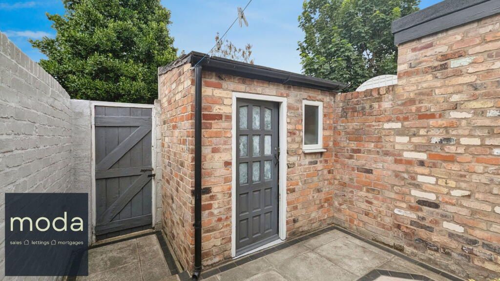 Small brick outbuilding with gray door, window, and adjacent wooden gate in an outdoor setting.