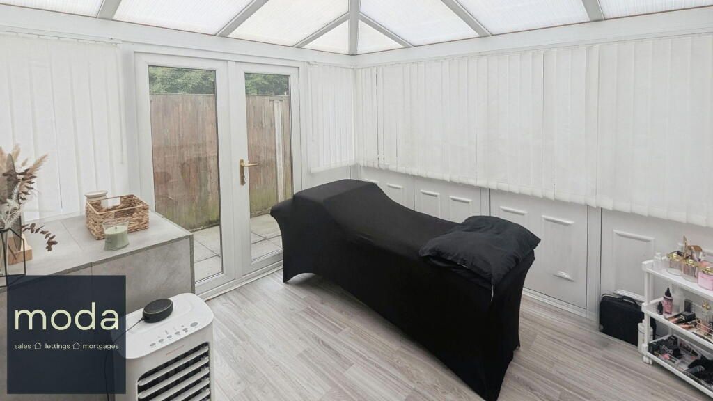 Spa room interior with a black chaise lounge, a side table, and cabinets. White walls and vertical blinds.