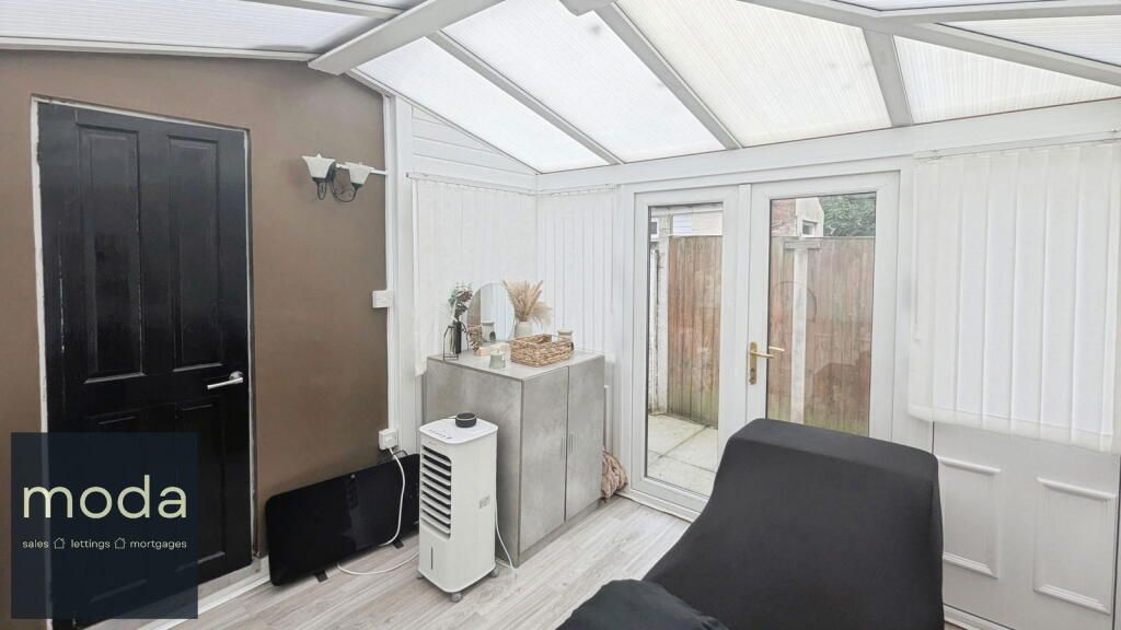 A sunroom with black door, white walls and ceiling, a black chair, and an air cooler. French doors lead outside.