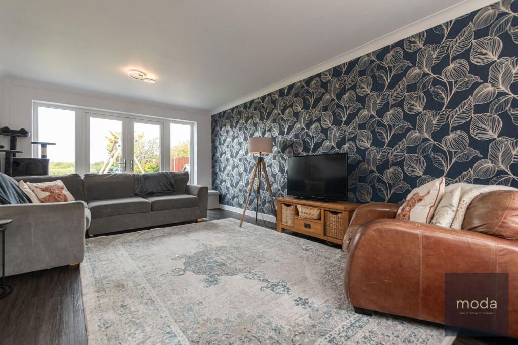 Living room with grey sofa, patterned rug, blue wallpaper, and brown leather chair.