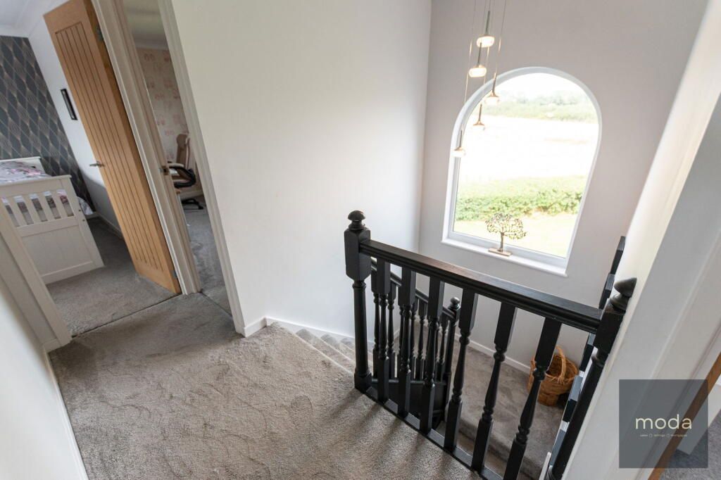 A hallway landing with a black bannister, arched window, and bedroom door, all brightly lit.