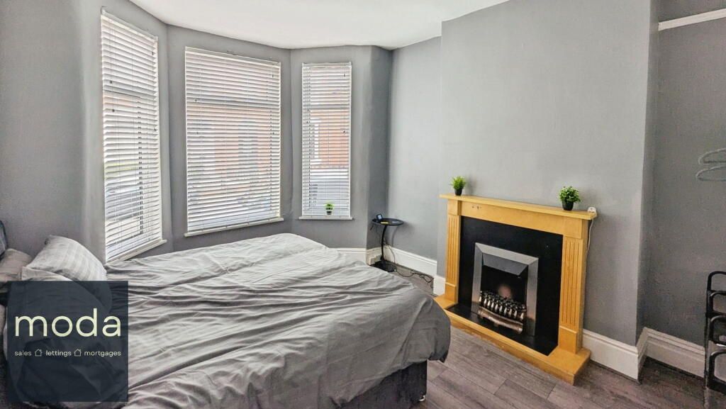 Bedroom with gray walls, bed, fireplace, and bay windows with blinds.