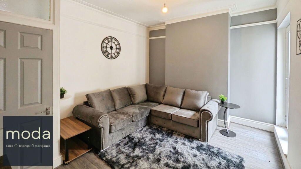 Cozy living room with grey sectional sofa, shaggy rug, and a decorative clock on the wall.