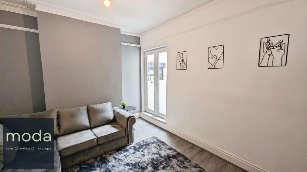 Living room with gray sofa, gray walls, rug, and black art. French doors open to outside.