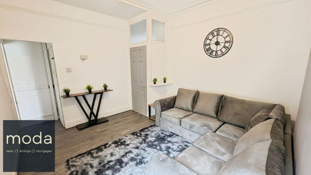 A living room with gray sectional sofa, rug, clock, and small table with plants.