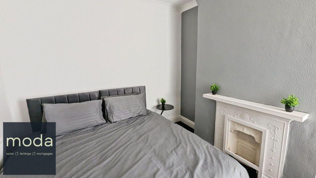 Gray bedroom with a bed, fireplace, and small plants.