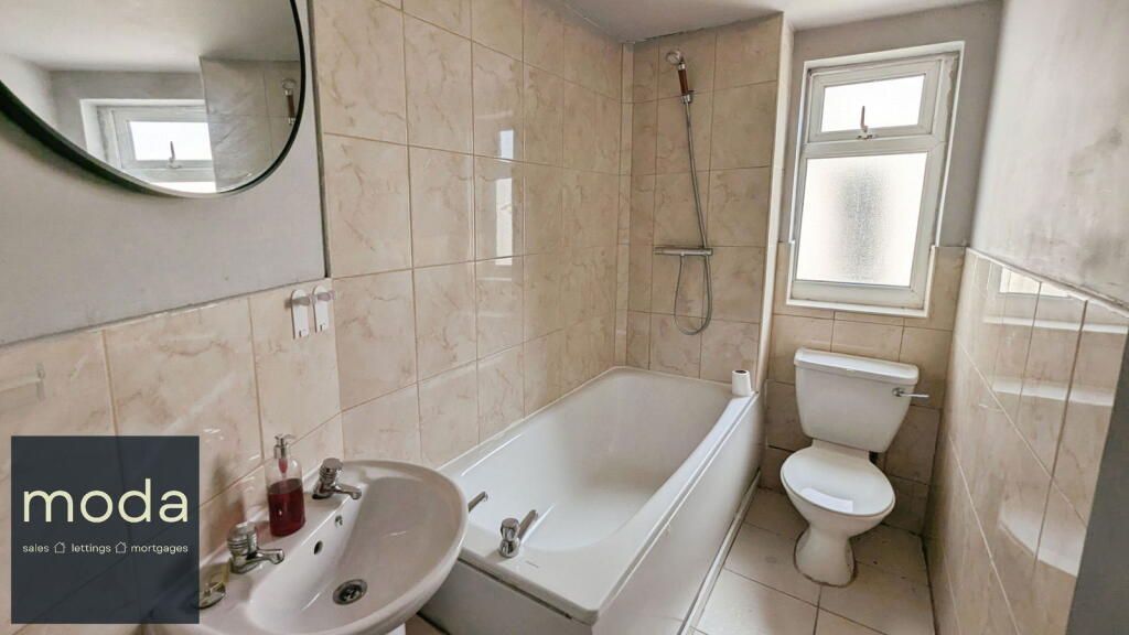 Bathroom with white fixtures, beige tile, and a window.