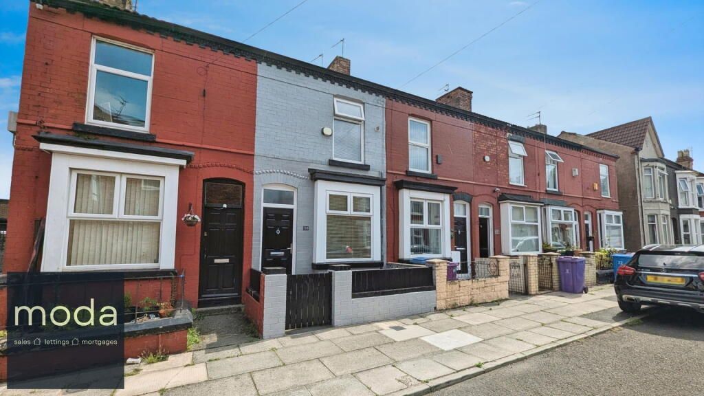 Row of terraced houses with red and gray exteriors on a paved street, under a blue sky.