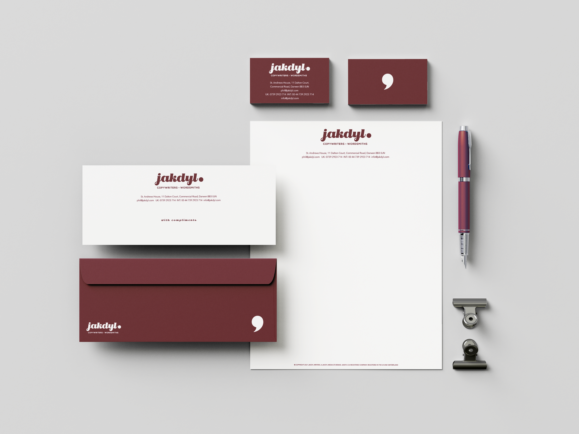 Business stationery set in burgundy and white: cards, letterhead, pen, and stamp on a light gray background