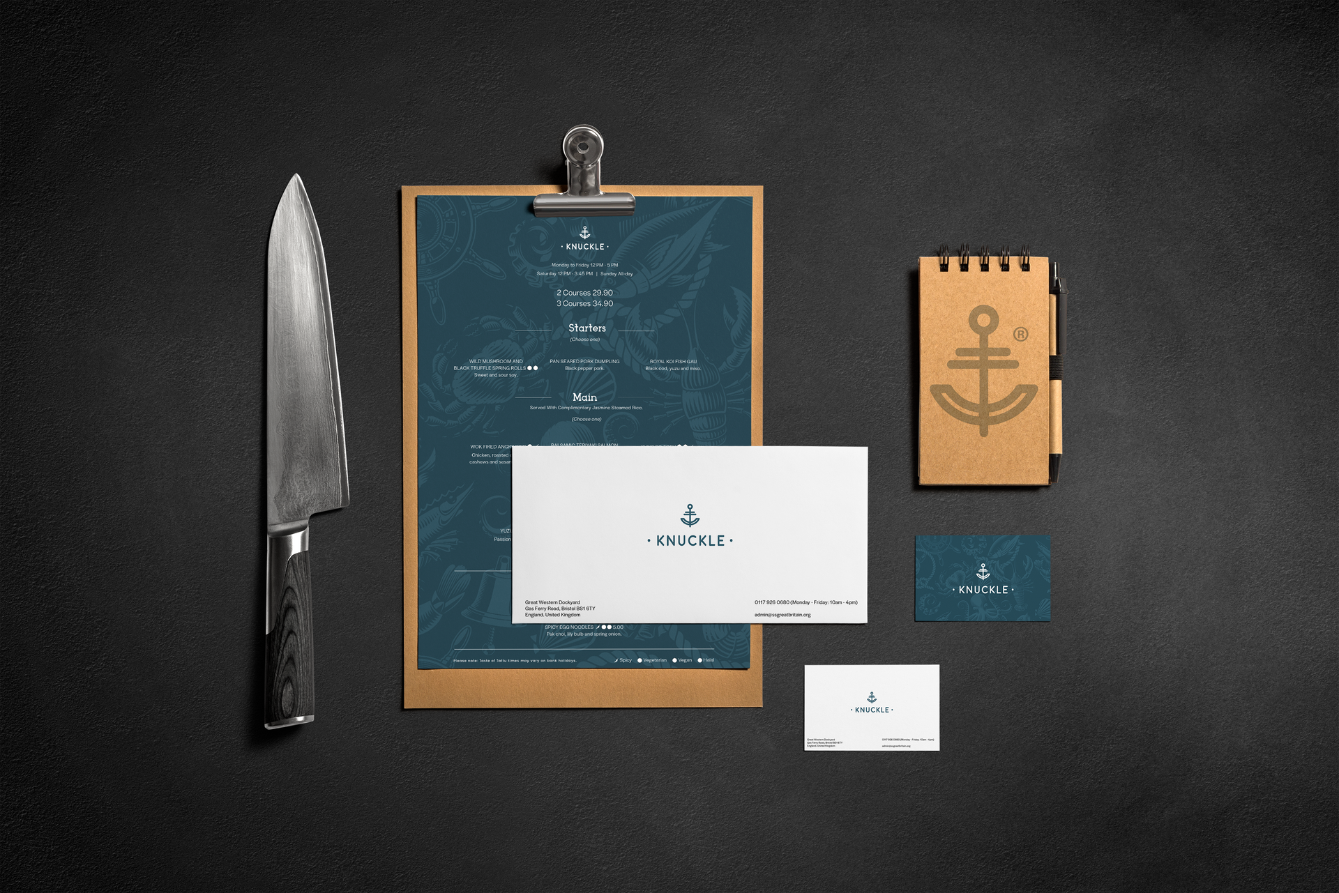 Knife, teal notebook, and small paper cards arranged on a dark textured background.