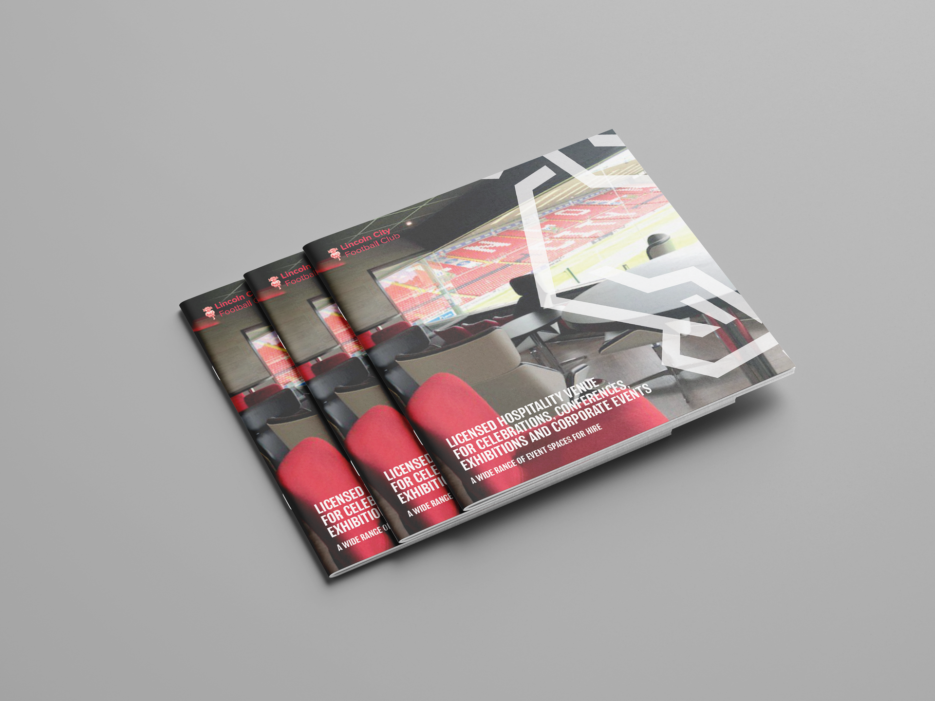 Stack of black-and-red brochures with a car on the cover, arranged on a light gray surface.