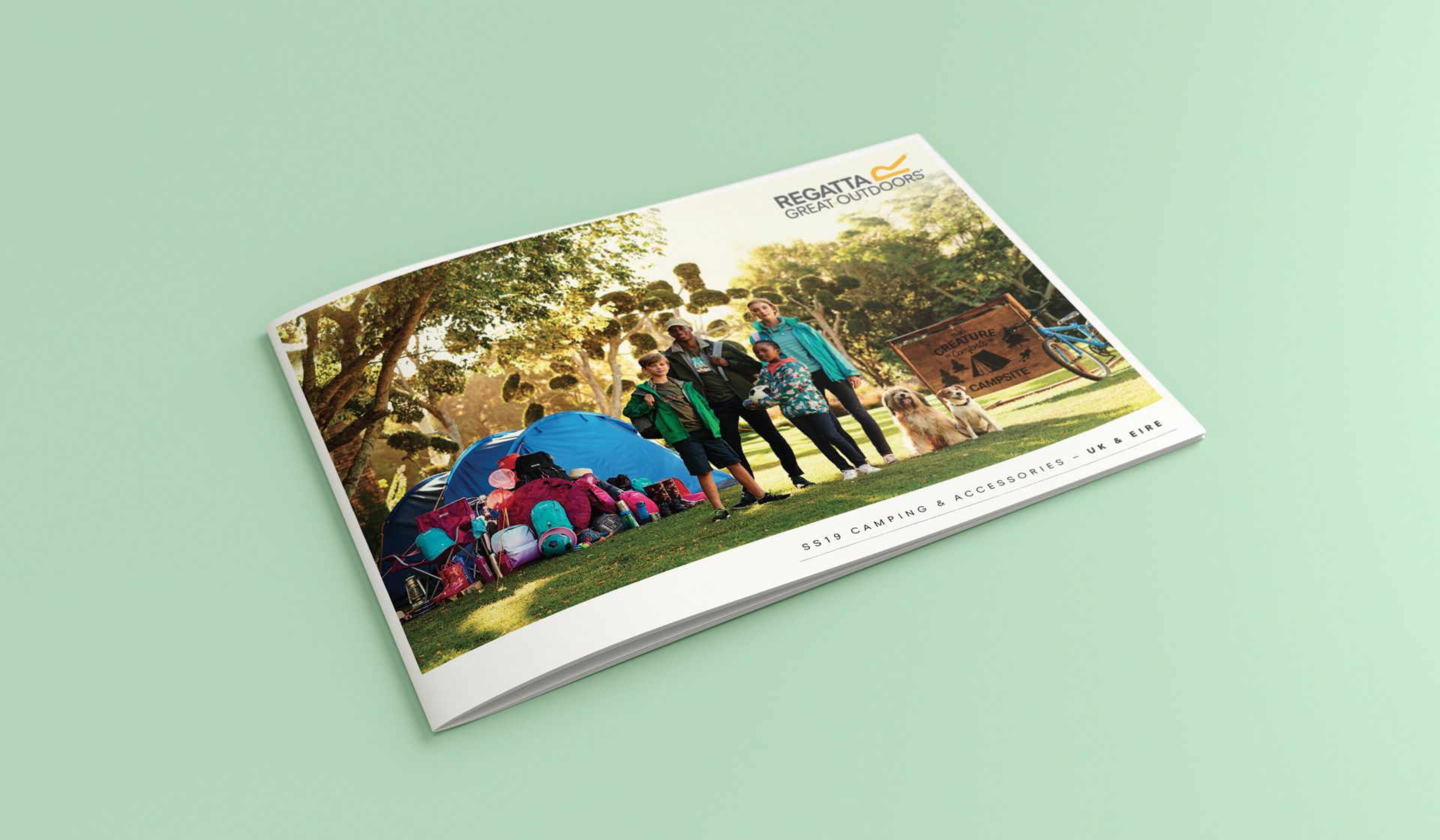 Small photo book on a mint-green background, showing people camping outdoors under trees.