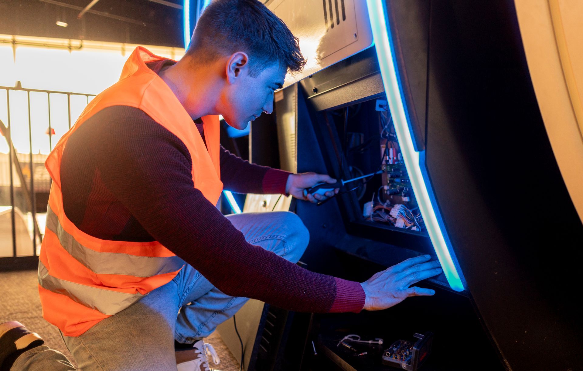 Technician repairing internal wiring of an arcade machine.