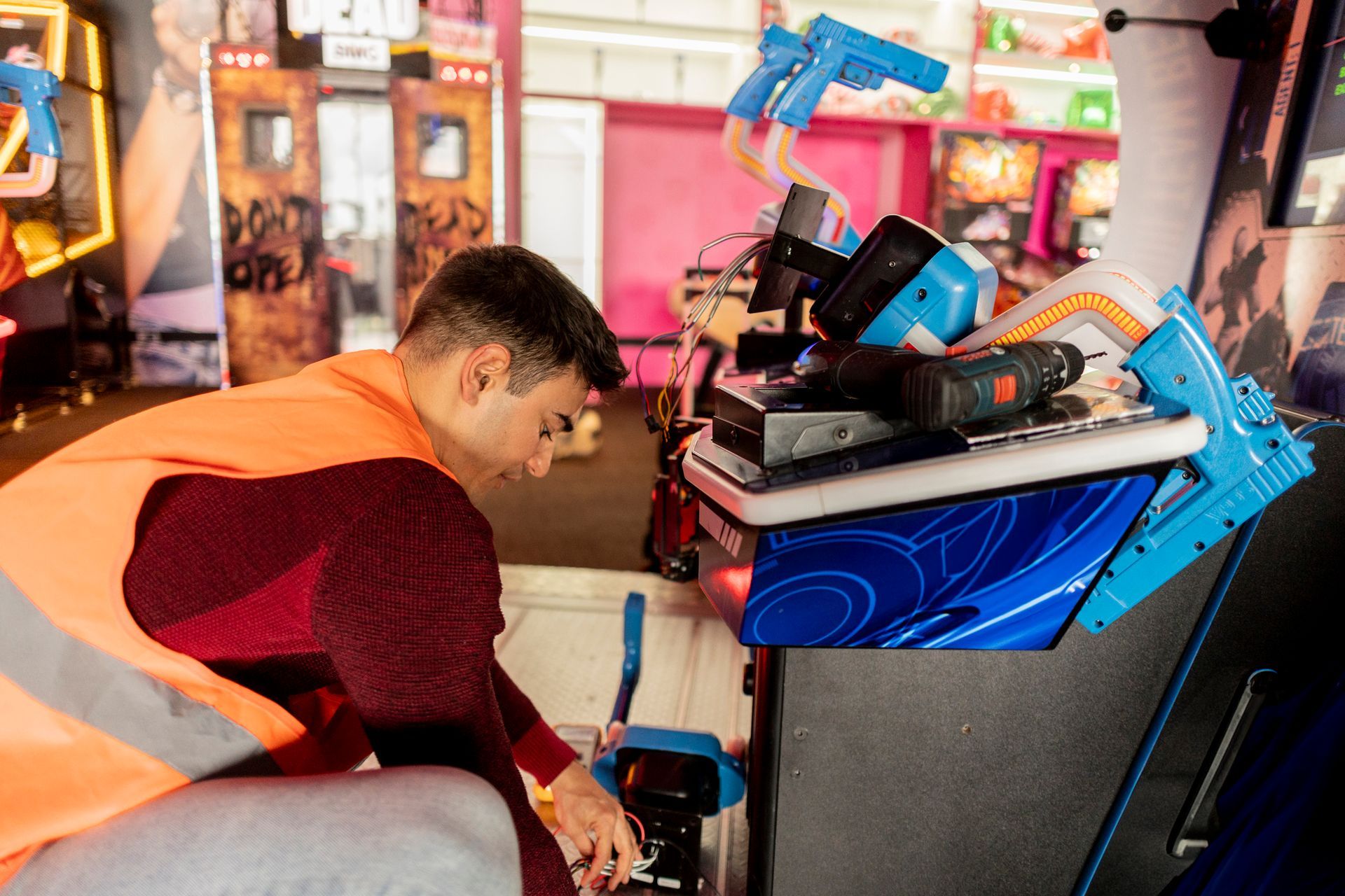 A man in an orange vest repairs a game machine, showcasing expertise in residential arcade repairs.