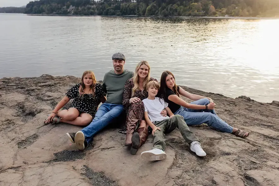 Five people sitting on rocks by a lake at sunset, relaxing with trees in the background.