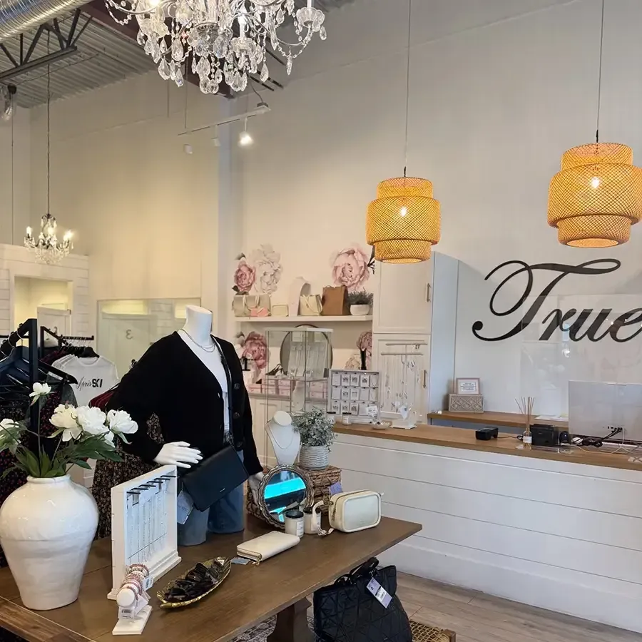 Boutique interior with white dresser, mannequins, floral decor, chandeliers, and woven pendant lights