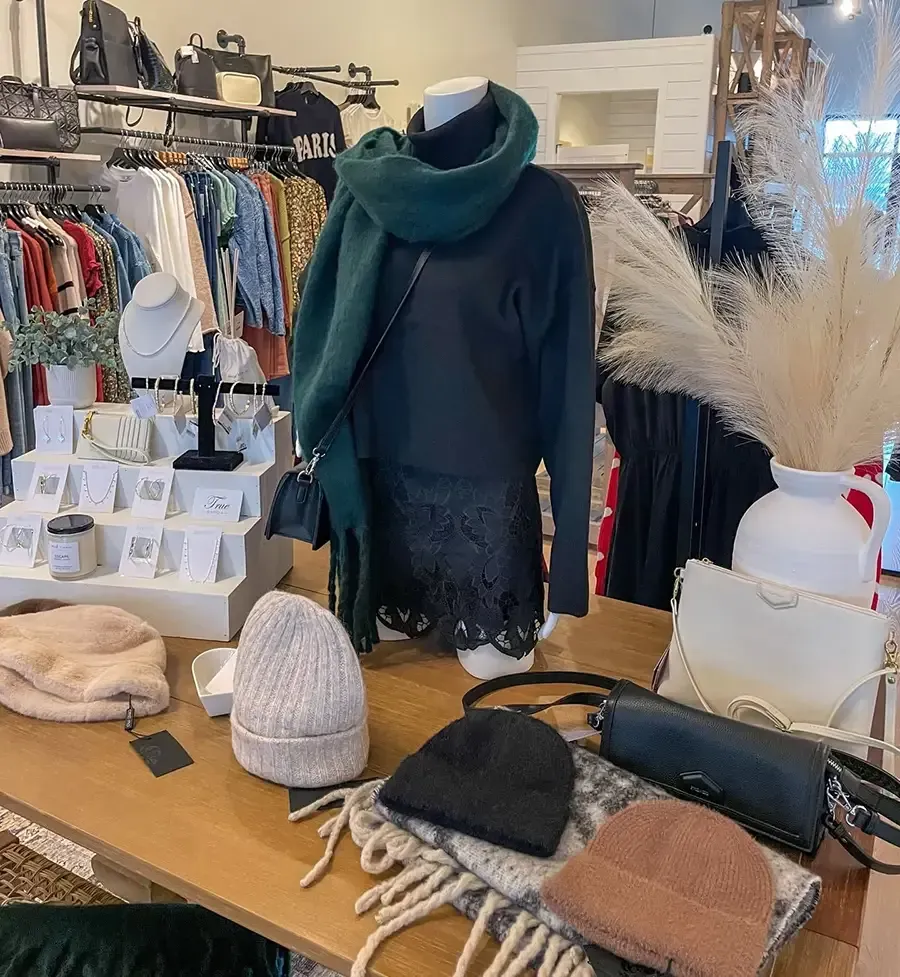 Clothing boutique display with dark sweater, teal scarf, hats, and accessories on a table