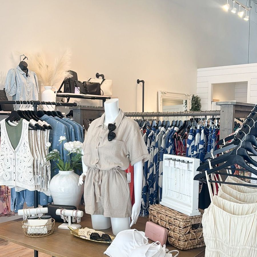 Boutique clothing display with neutral-toned dresses, racks of apparel, and woven baskets in a bright shop interior