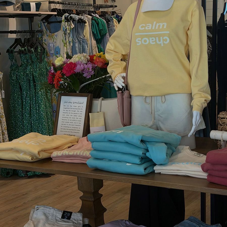 Clothing store display with folded pastel sweatshirts on a table and a mannequin in a yellow sweatshirt.