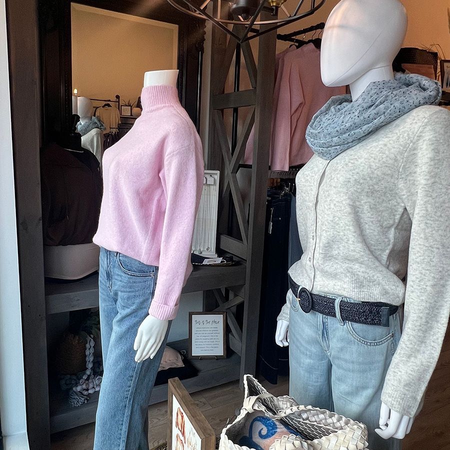 Store mannequins wearing a pink sweater and gray sweater with scarf, jeans, and belt