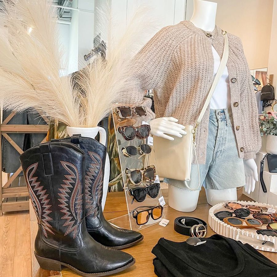 Boutique display with black cowboy boots, beige cardigan, jeans, sunglasses, and accessories on mannequins