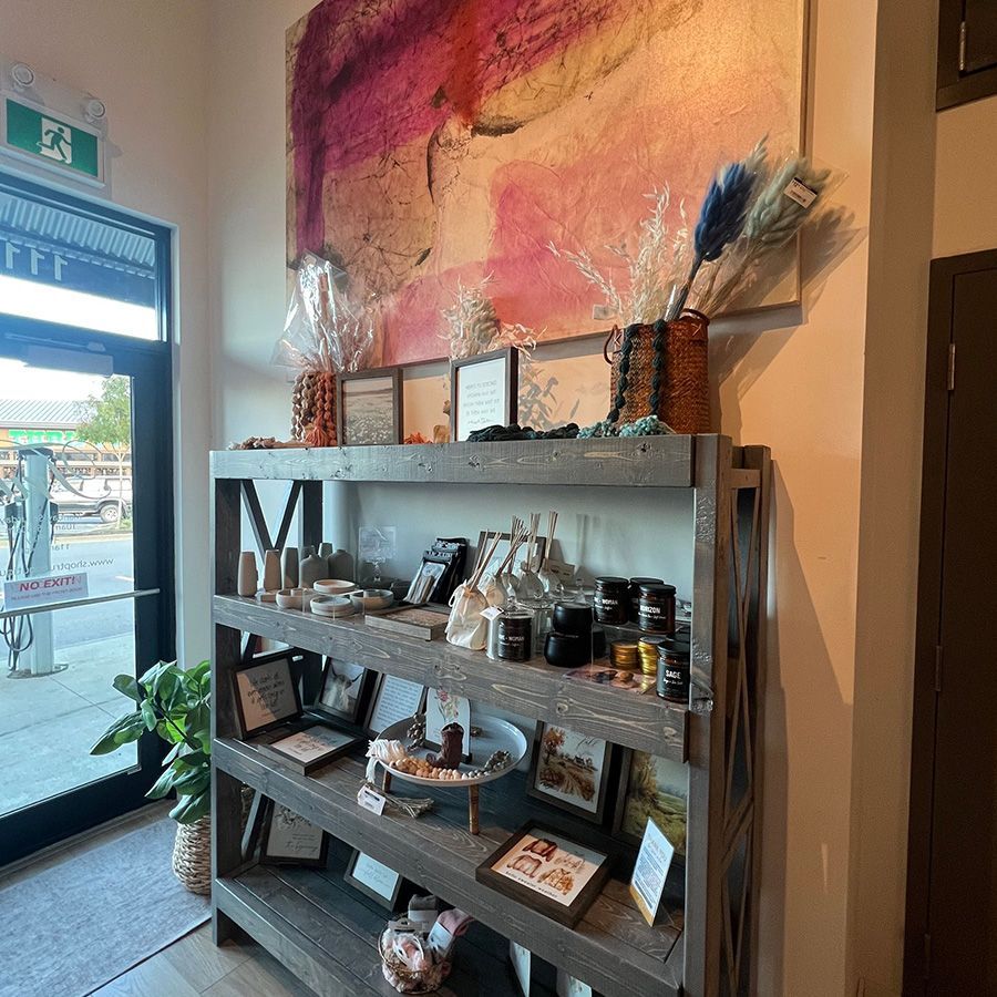 Shelved shop display with jars, framed art, and dried floral arrangements by a glass entrance