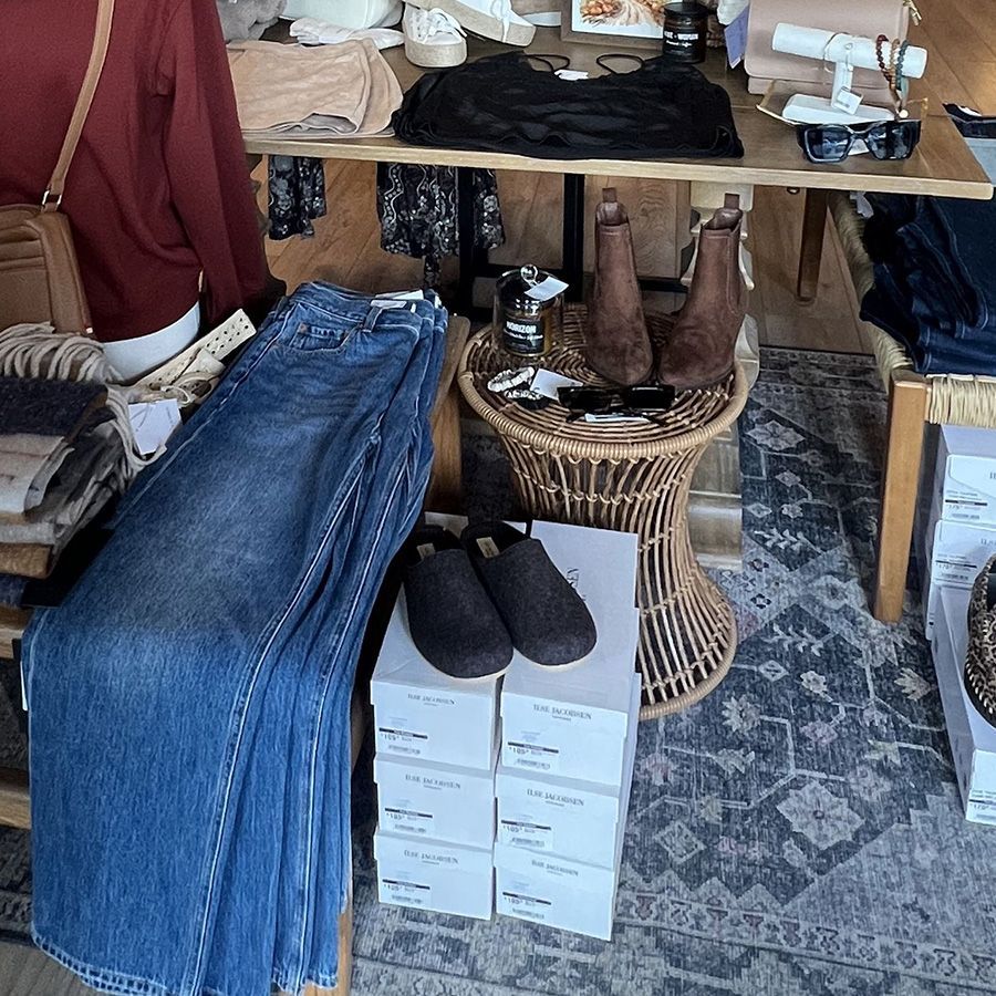 Clothing shop display with folded jeans, black shoes on stacked boxes, and a wicker table with accessories