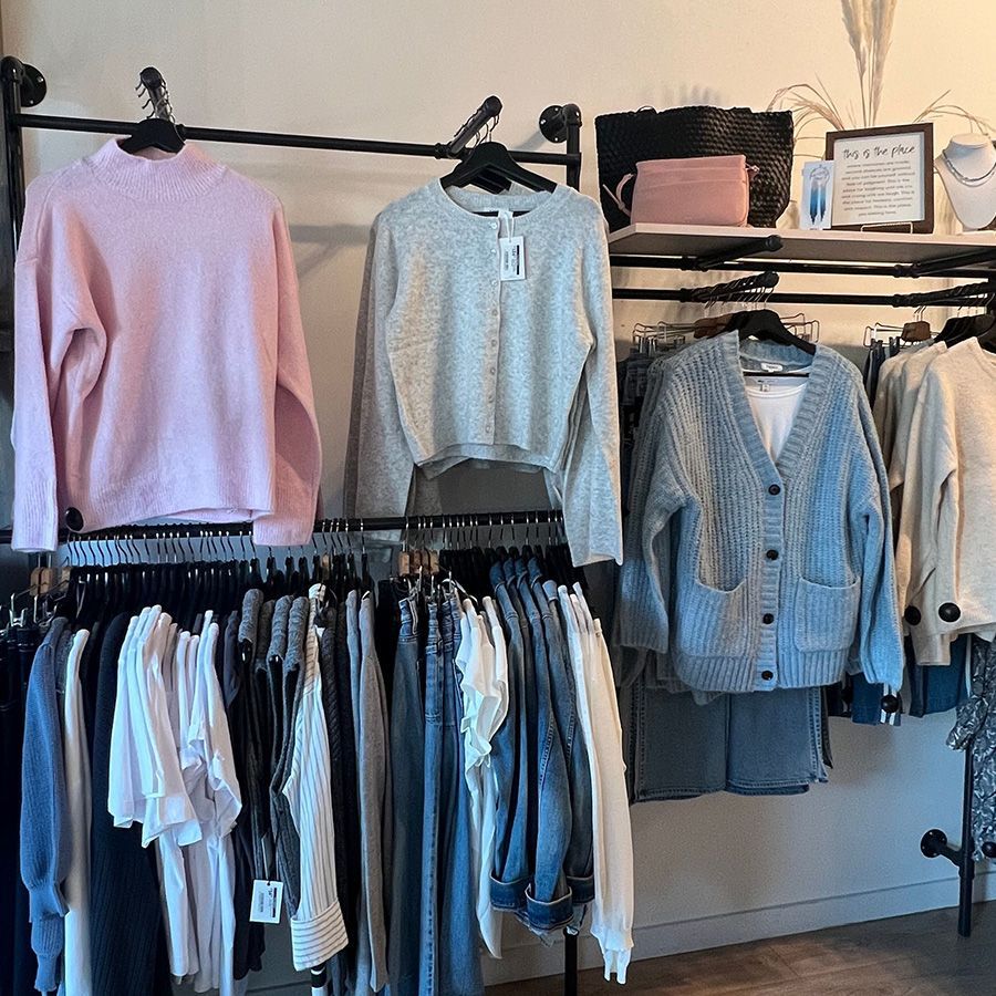 Clothing rack in a boutique with sweaters, cardigans, and jeans in pastel and neutral colors