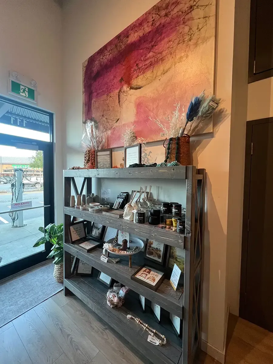 Display shelf with assorted home decor in a bright shop entrance beneath a colorful wall hanging