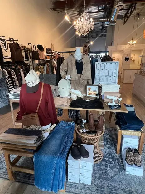 Boutique display with folded denim, sweaters, shoes, and accessories on tables in a clothing store